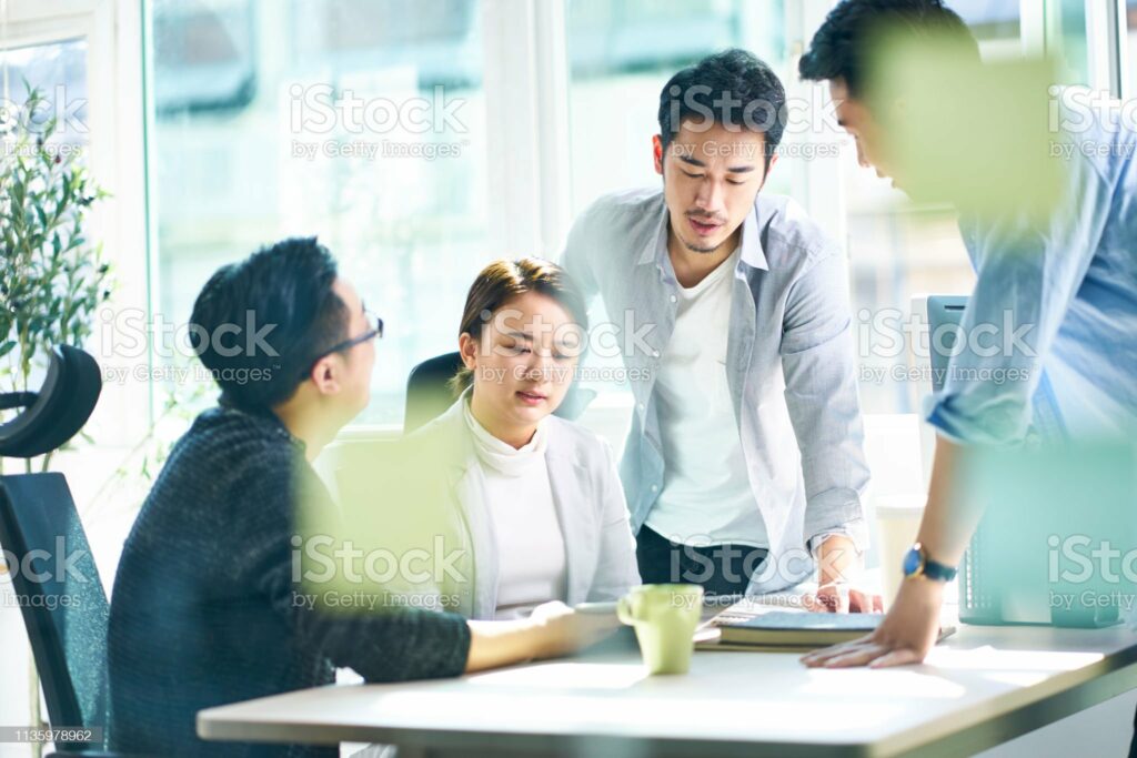 group of four young asian corporate executives meeting in office discussing business in office.